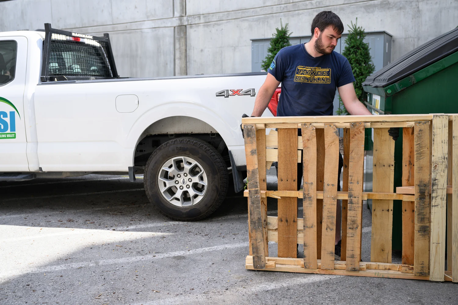 A Bulk Away crew member moving a wooden pallet beside a WSI service truck and a dumpster