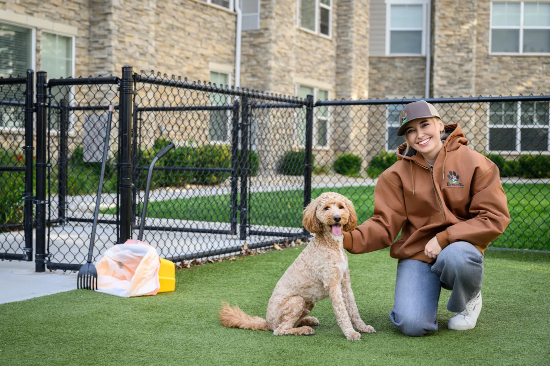 A Pet Waste Pals team member kneeling with a dog on the turf of a fenced community dog park